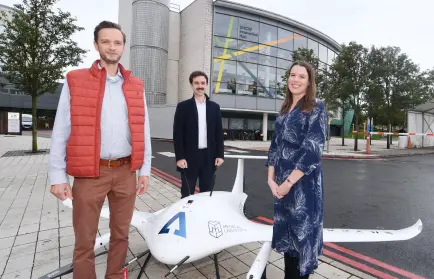 Three people standing next to a big medical drone