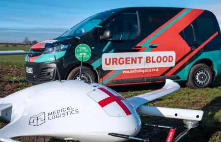 A black electric car with red and mint stripes next to a white drone with a medical logistics logo